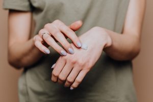 Crop anonymous female in casual shirt with manicured hands and ring softly rubbing hand moisturizer in back of hand skin