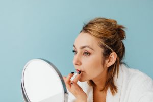 A Woman Applying a Cream on Her Lips while Looking at the Mirror