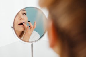 A Woman Looking at the Mirror while Applying a Cream on Her Lips